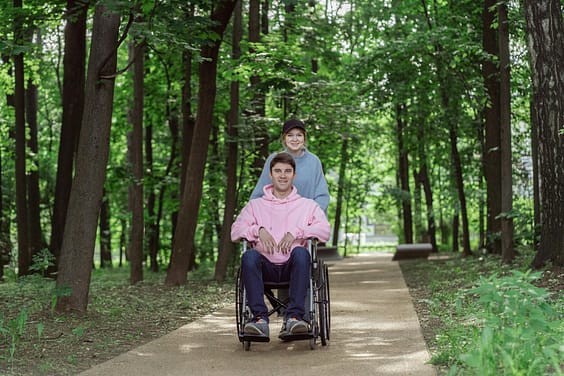 pexels-photo-8415822-8415822 Smiling couple enjoying a sunny day in a park. Man in a wheelchair being pushed by a woman.